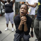 Un hombre reza mientras la policía dispersa a los manifestantes en Ferguson tras el asesinato de Michael Brown.