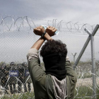 Un refugiado permanece tras la valla fronteriza frente a un grupo de policías macedonios. K. TSIRONIS