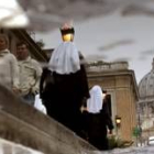 Dos monjas caminan a lo largo de la Via della Conciliazione vistas a través del reflejo de un charco