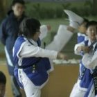 Un joven practicante de tae kwondo trata de romper la tabla que sujetan dos de sus compañeros