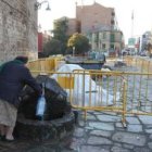 Una mujer coge agua del caño actual; detrás, tapada, la nueva fuente de la plaza.