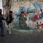 Palestinos pasan delante de un muro en el que hay un graffiti con un miembro de Hamás, en Gaza