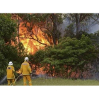 Dos bomberos intentar extinguir las llamas de un incendio declarado en la bahía de Catherine Hill, en Nueva Gales del Sur, este viernes.
