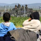 Varios niños descansan junto a la valla fronteriza mientras la policía macedonia hace guardia. XHEMAJ