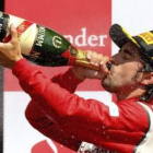 El piloto español de Fórmula 1 Fernando Alonso, de la escudería Ferrari, bebe champagne en el podio