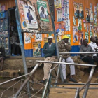 Un grupo de kenianos junto a un local con la fachada cubierta de carteles durante la campaña electoral