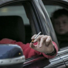 Un conductor fuma un cigarrillo en un coche, con un niño en el asiento de atrás.