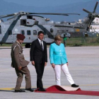 Renzi, Merkel y un oficial tratan de ajustar la alfombra roja en el aeropuerto de Nápoles, antes de desplazarse a Ventotene.