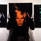 Un empleado de la casa de subastas Christie's presenta tres autorretratos del artista estadounidense Andy Warhol, durante su presentación a la prensa antes de salir a la venta, en Londres en 2018. WILL OLIVER