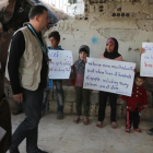 Niños sirios sostienen pancartas reivindicativas frente a miembros de un convoy de ayuda humanitaria durante una entrega de material en Al-Nashabia, en la región de Guta Oriental, al este de Damasco, el 28 de noviembre.