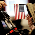 Imagen muestra a un bebe que intenta alcanzar la bandera estadounidense que sostiene su madre en Nueva York.