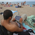 Un joven, con una tablet en la playa de la Barceloneta, en julio.