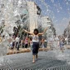 Una niña combate el calor al pasar bajo los surtidores de una fuente en Alicante