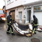 Dos bomberos sacan del interior de la casa uno de los colchones calcinados.