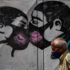 Un hombre camina frente a un grafiti que muestra una pareja besándose con mascarillas. MIGUEL GUTIERREZ