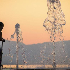 Una niña se refresca en una fuente.