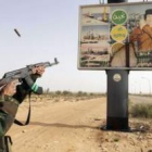 Un rebelde libio dispara contra una valla publicitaria con la imagen del coronel Muamar El Gadafi.