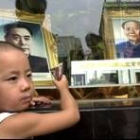 Un niño come un helado delante de los retratos de Zou Enlai y Mao