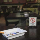 Un cigarro, junto a un cartel que indica la prohibición de fumar en una cafetería.