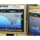 Un hombre observa las pantallas con la evolución del IBEX 35 (izquierda) y el diferencial con el bono alemán (derecha).