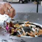 Una mujer apaga un cigarrillo en una papelera callejera