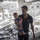 Un palestino camina con su hijo en brazos sobre los escombros de la que era su casa.
