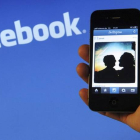Un usuario de smartphone, delante de un logotipo de Facebook.
