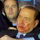 Berlusconi, con la cara ensangrentada, es ayudado por sus escoltas tras la agresión.