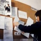 Una joven consulta los anuncios de oferta de trabajo situados en un tablero en una oficina del Inem