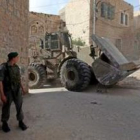 Soldados israelíes hacen guardia mientras una retroexcavadora mueve un bloque de piedra en la ciudad