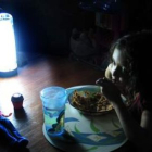 Una niña come alumbrada por una lámpara.