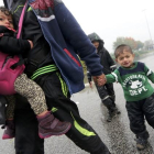 Un hombre camina llevando a dos niños bajo la lluvia junto a la frontera con Eslovenia.