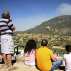 Varias personas contemplan un helicóptero que lleva agua para arrojar sobre el incendio.