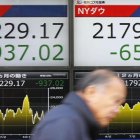 Un hombre pasa ante un cartel que exhibe las pérdidas del índice Nikkei, a la izquierda, y del Dow Jones, en una firma de valores en Tokio