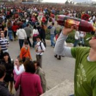 Un joven, en primer término, bebiendo de una botella durante la celebración de un multitudinario bot