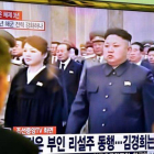 Dos personas miran en una gran pantalla de televisión la retransmisión de la ceremonia de conmemoración, en una estación de trenes de Seúl (Corea del Sur).