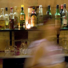 Una mujer, delante de la barra de un bar llena de bebidas