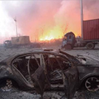 Vista de un coche calcinado en la seria de explosiones de unos almacenes de Tianjin, en China. En segundo plano, el fuego sigue ardiendo.