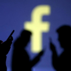 Unos usuarios de Facebook, ante el logotipo de la red social.