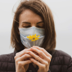 Mujer con mascarilla anti-alérgica observando una flor.