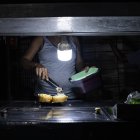 Una persona vende comida ayudado con un bombillo en medio de la oscuridad durante un corte eléctrico, el 29 de febrero de 2024 en Maracaibo (Venezuela). EFE/ Henry Chirinos