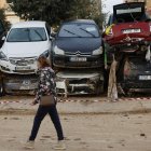 Una mujer pasa junto a decenas de coches que esperan ser retirados en Paiporta. EFE/Biel Aliño