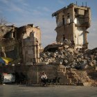 Un vendedor ambulante se sienta el 5 de diciembre de 2024 frente a un edificio dañado mientras la gente se reúne en el lado de la Ciudadela de Alepo (Siria), después de que la oposición tomó control de la ciudad. EFE/EPA/BILAL AL HAMMOUD