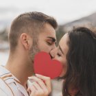Dos enamorados se besan tras el símbolo de un corazón.