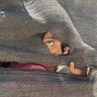Una niña se asoma tras una tienda improvisada en el puerto en la Ciudad de Gaza, donde miles de personas desplazadas por los ataques israelíes han encontrado refugio, el 20 de mayo de 2025. EFE/ Ahmad Awad.