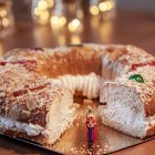 Detalle de un roscón de Reyes tradicional con nata, decorado con almendras y frutas confitadas, junto a la figura del rey escondida en su interior.