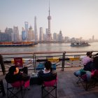 Un grupo de personas en una cafetería observan el paso de barcos de carga por el río Huangpu, en Shanghái.