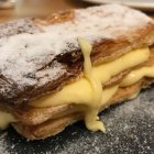 La clásica milhojas de crema, con capas doradas de hojaldre y relleno generoso que se desborda, símbolo del dulce tradicional de La Bañeza y León