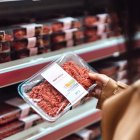 Una mujer observa el etiquetado de carne envasada en un supermercado