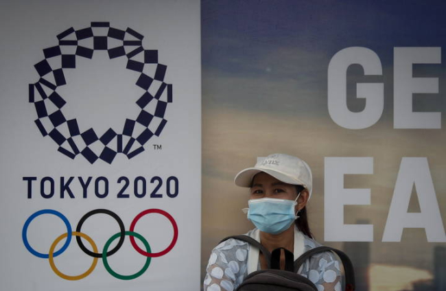 Una mujer en Bangkok, junto al cartel de los Juegos de Tokio, que se han aplazado a 2021. DIEGO AZUBEL